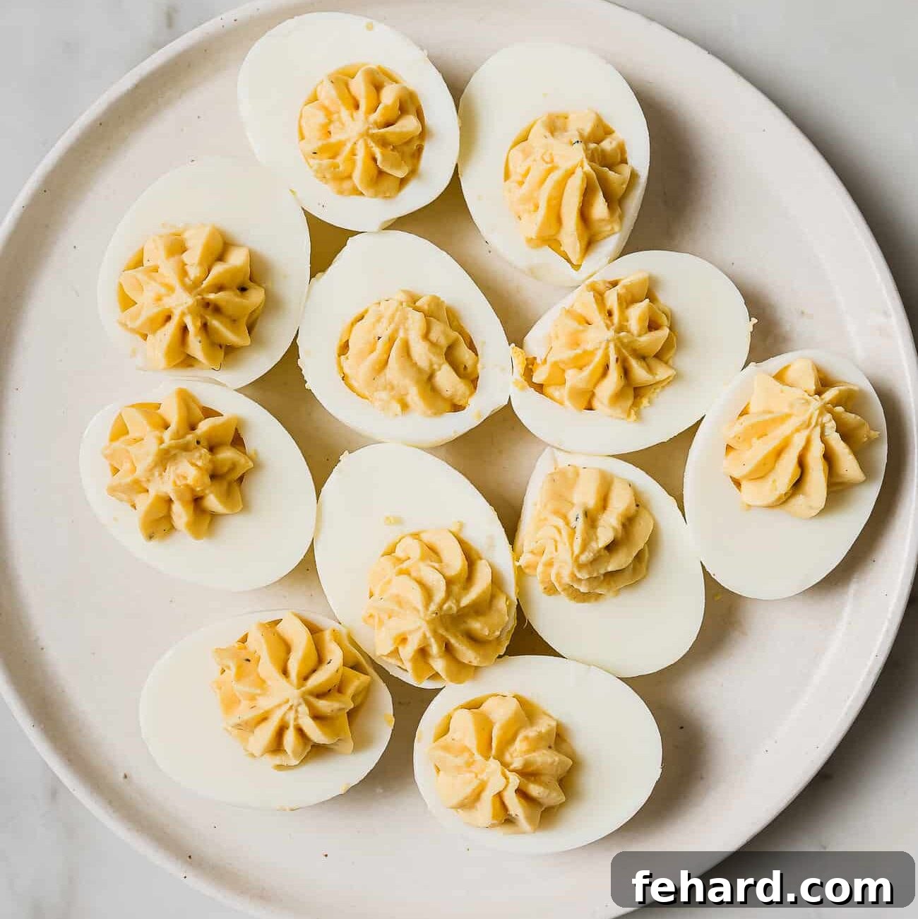 Beautifully filled deviled eggs garnished with paprika, bacon, and fresh chives, arranged artfully on a white plate, ready to be served.