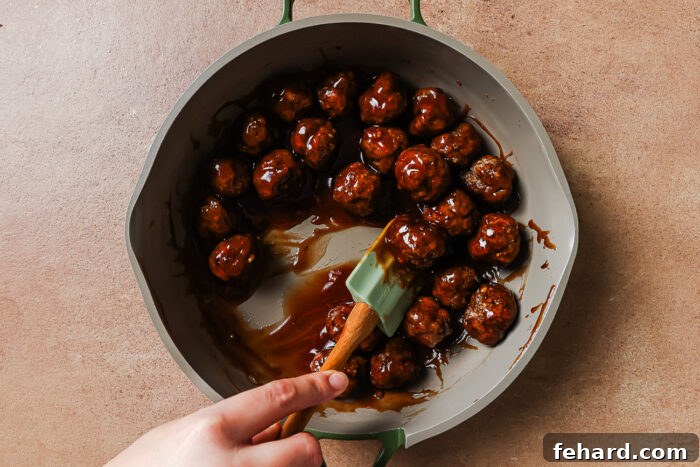 Irresistible Party Meatballs 9 Cocktail meatballs simmering in sauce in a skillet.