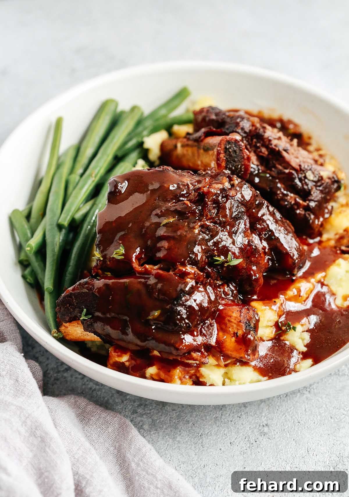 Overhead view of a bowl containing perfectly cooked Instant Pot Short Ribs, garnished with fresh herbs.