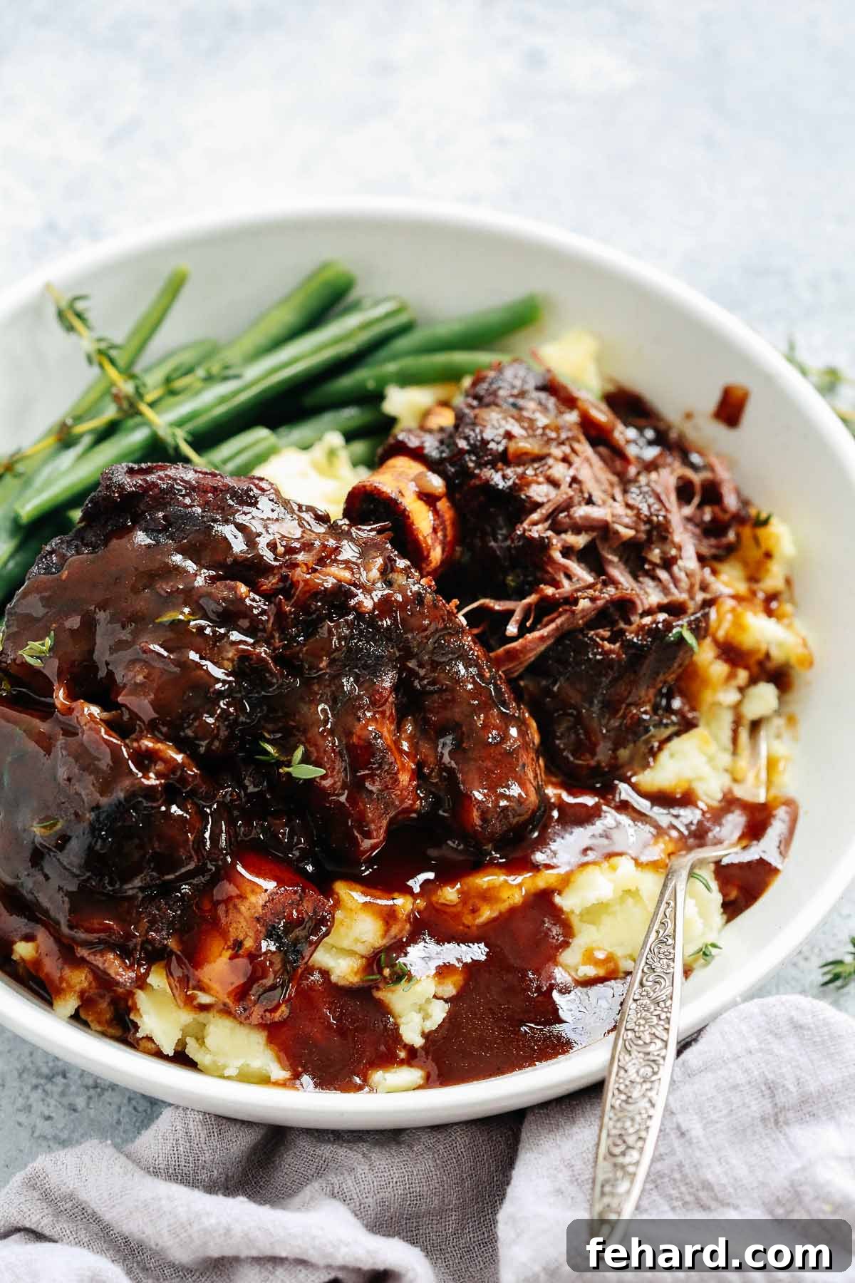 A close up of tender short ribs served with vibrant green beans and creamy mashed potatoes in a white bowl.