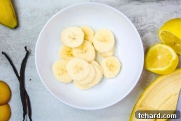 Sliced bananas in a white bowl being dipped in lemon juice.