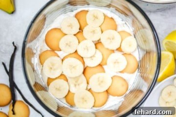 Layered vanilla pudding with vanilla wafers and sliced banana in a trifle dish during assembly.