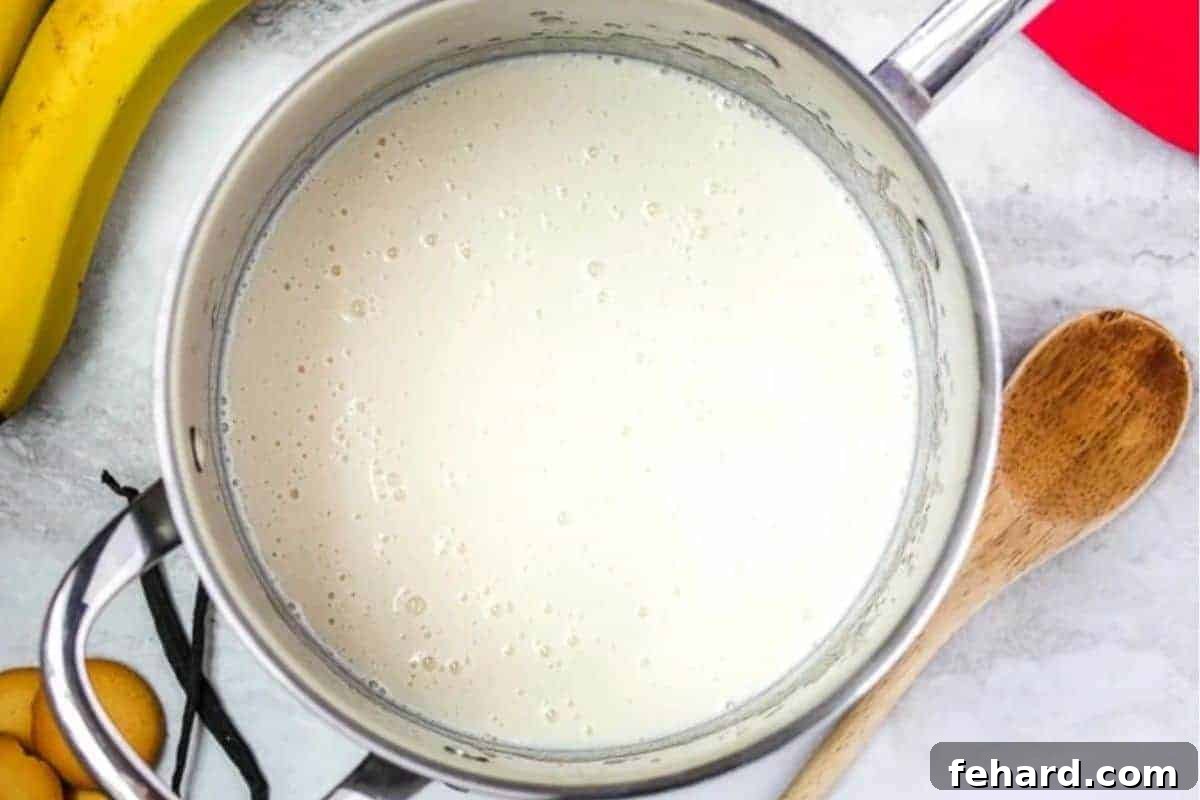 Homemade vanilla pudding simmering in a saucepan, next to fresh vanilla wafers and ripe bananas.