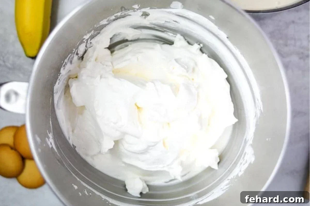 Freshly whipped heavy cream in a large stainless steel KitchenAid mixing bowl, ready to be folded into pudding.