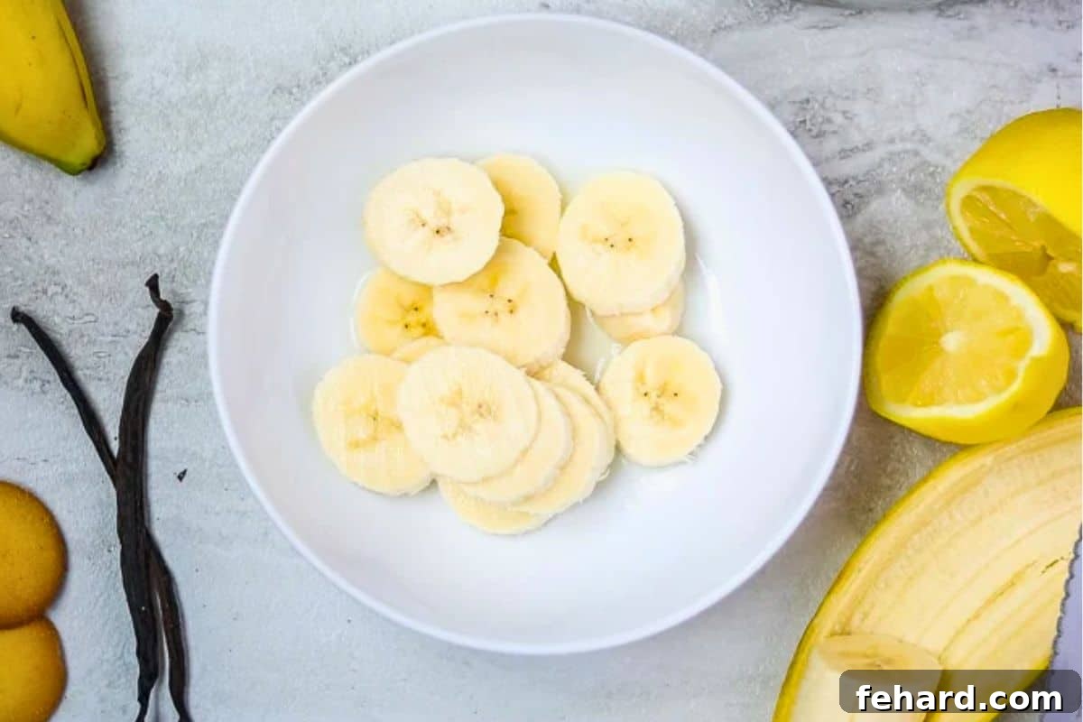 Sliced bananas in a white bowl being dipped in lemon juice to prevent browning and add a tart flavor.
