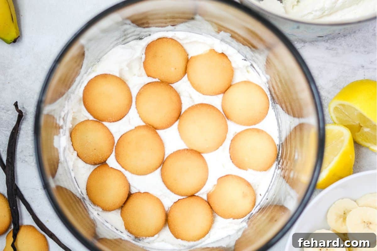 First layer of vanilla pudding with vanilla wafers in a clear trifle dish, showcasing the dessert's structure.