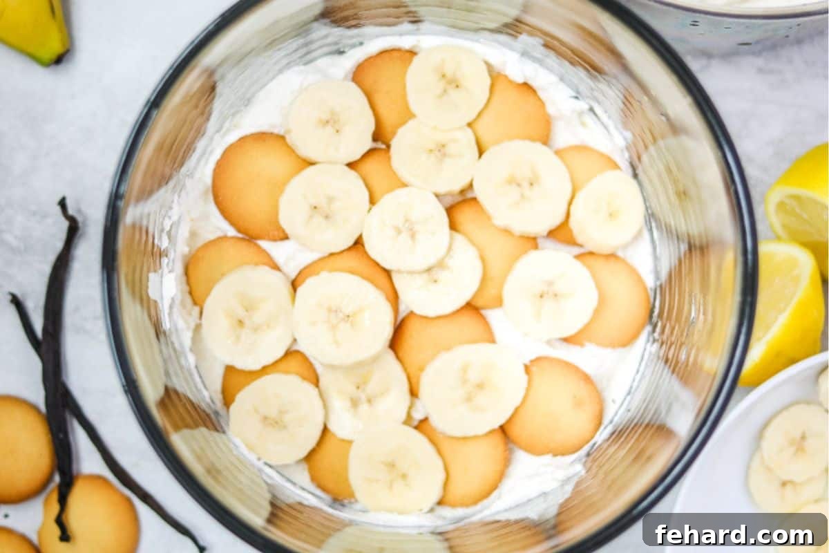 Second layer of vanilla pudding with vanilla wafers and fresh banana slices in a trifle dish.
