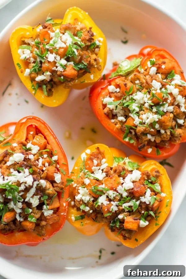 Four ground turkey sweet potato stuffed peppers inside of a large serving bowl, garnished with fresh herbs.