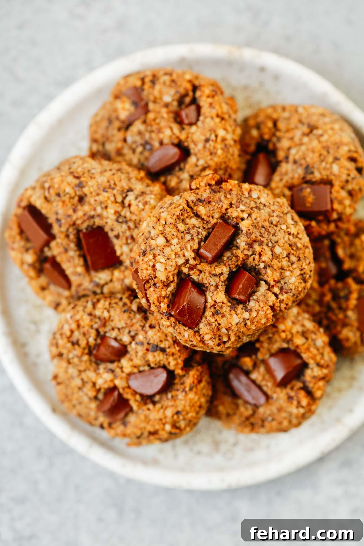 A white plate generously filled with multiple golden-brown chocolate chunk hazelnut cookies, ready to be enjoyed.