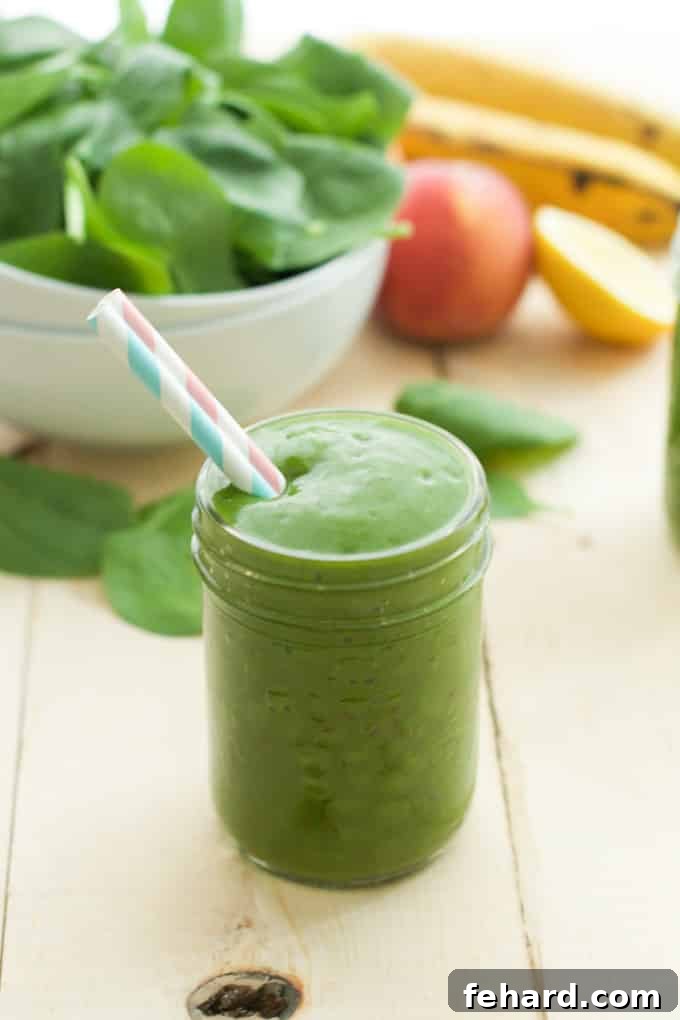 Close up of a green smoothie in a mason jar with a straw, emphasizing its vibrant color and texture.