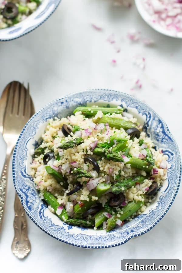 A bowl of Asparagus Couscous Salad with a fork and spoon beside it on a rustic table setting.