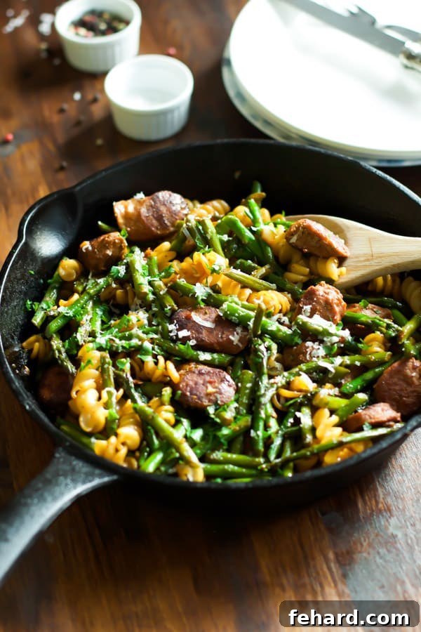 A comforting cast iron skillet filled with sausage, asparagus, and quinoa pasta.