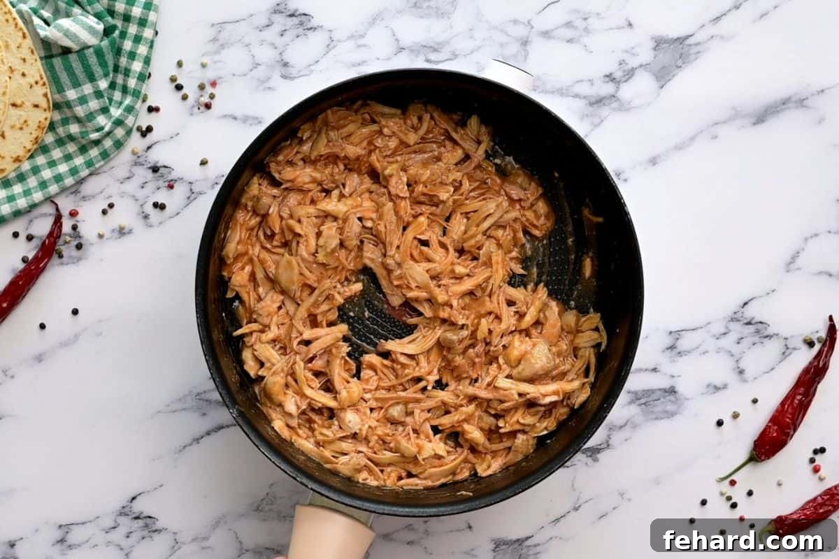 Buffalo Chicken Coating Shredded chicken tossed with buffalo sauce in saucepan.