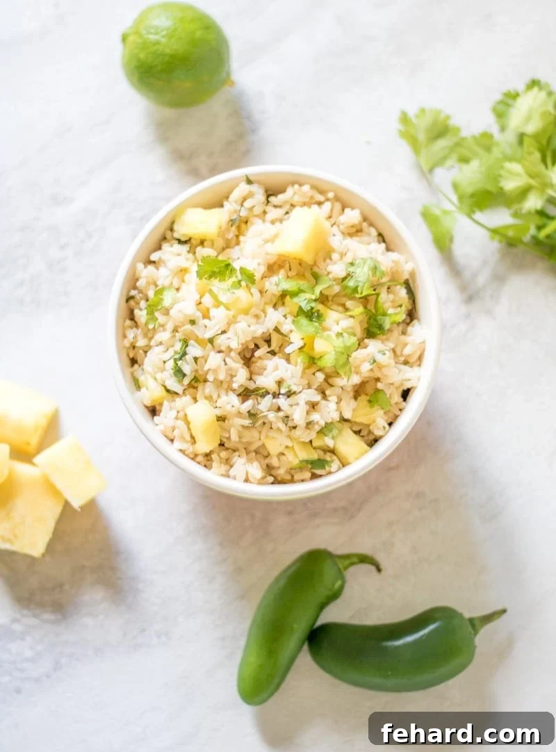 A serving of Pineapple Cilantro Lime Rice in a white bowl, garnished with fresh lime wedges and cilantro sprigs, on a clean white counter.
