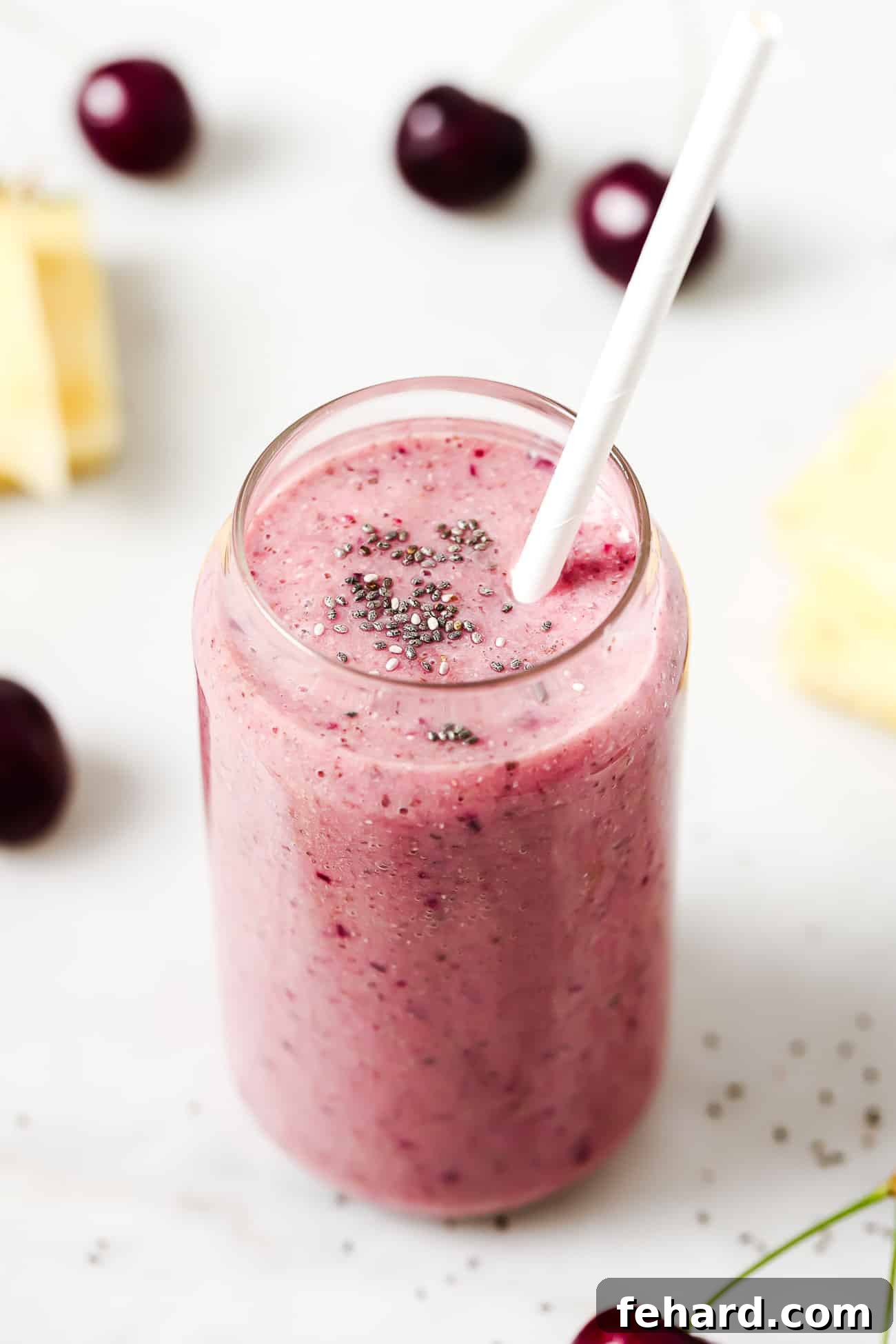 A cherry smoothie in a glass with chia seeds and a white straw.
