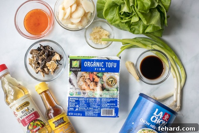 Fresh ingredients for making vegan lettuce wraps displayed neatly on a white kitchen counter, including tofu, mushrooms, lettuce, and sauce components.