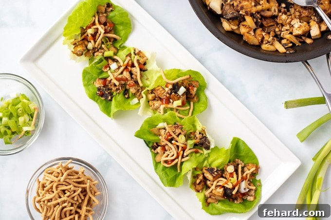 A beautifully arranged platter of finished vegan lettuce wraps, artfully placed next to a sauté pan filled with the savory tofu and mushroom mixture, ready for serving.