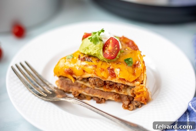 A tempting slice of Mexican Lasagna on a pristine white plate, beautifully topped with fresh tomato and a dollop of guacamole, ready to be enjoyed.