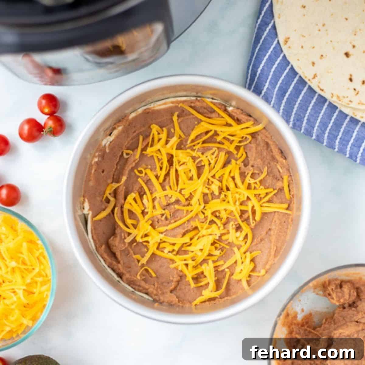 A tortilla generously topped with refried beans and cheese, alongside the Instant Pot, illustrating the layering process.
