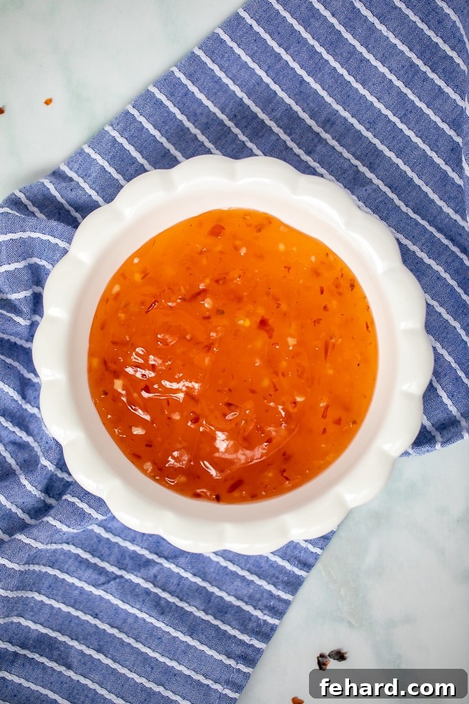 A pristine white bowl filled with homemade sweet chili sauce, garnished with a blue napkin in the background, ready for serving.