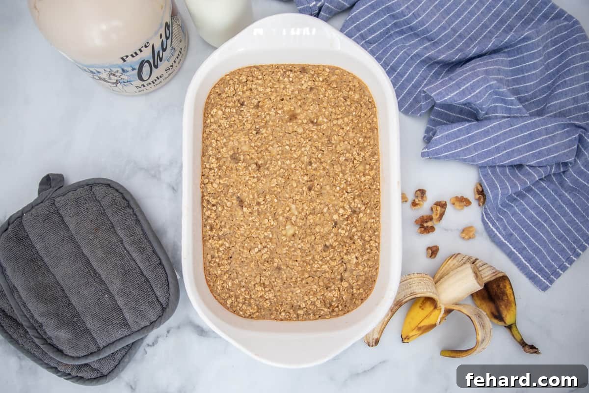 A charming casserole dish presents a freshly baked banana oatmeal, perfectly golden-brown and ready to serve. It's artfully arranged next to ripe bananas and a scattering of chopped walnuts, illustrating a delightful and easy one-bowl breakfast.