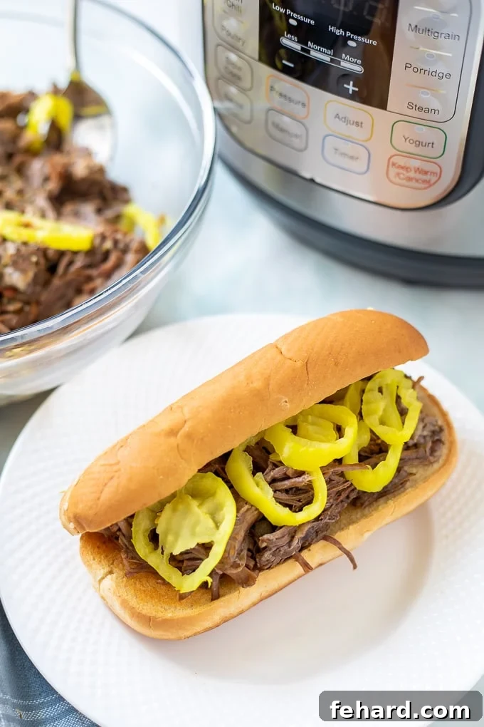 Instant Pot Italian Beef Recipe A bowl of shredded Instant Pot Italian Beef next to a classic Italian Beef Sandwich, with an Instant Pot in the background.