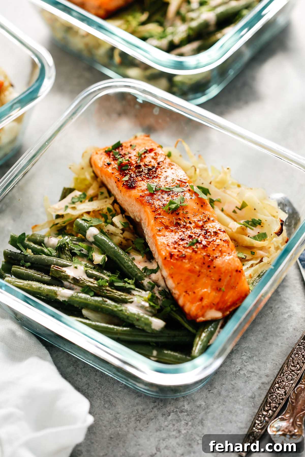 Broiled salmon filet with green beans and cabbage in a meal prep container, ready for a healthy lunch.