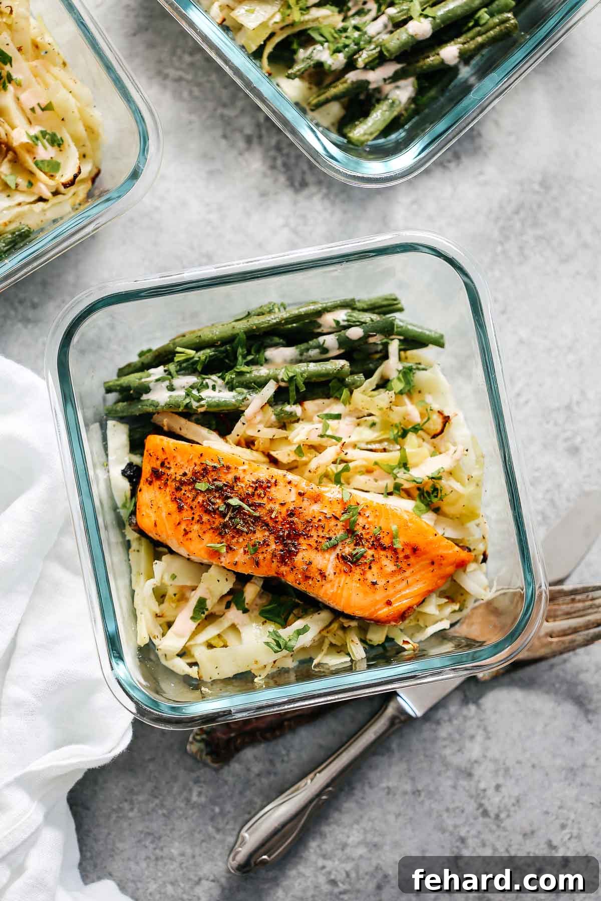 Close-up of a meal prep dinner featuring broiled salmon, seasoned green beans, and roasted cabbage.