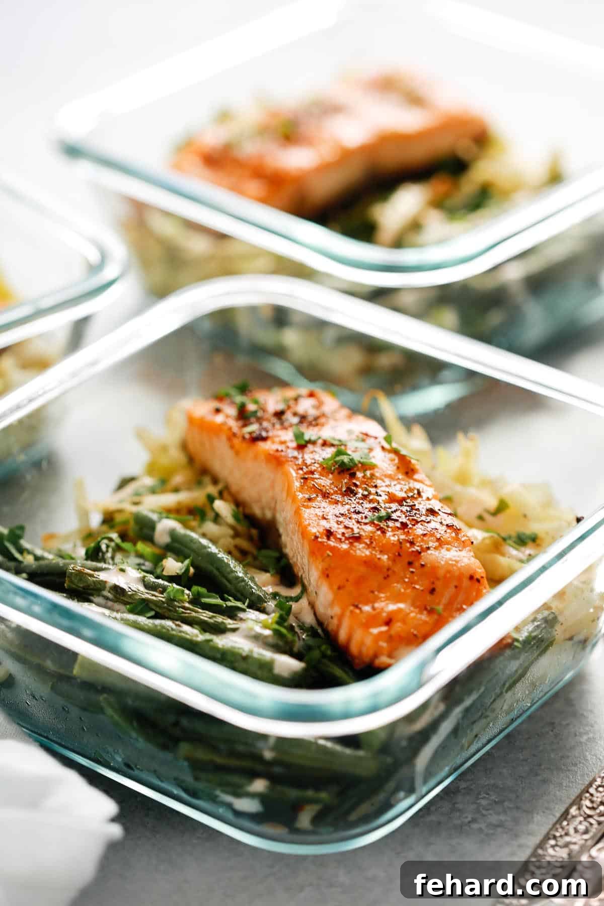 Broiled salmon filet, green beans, and cabbage neatly arranged in a square glass meal prep container.