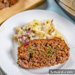 Slice of Instant Pot Meatloaf on white plate next to red smashed potatoes.