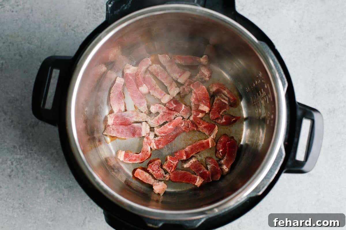 Strips of sirloin steak being browned in an Instant Pot, developing a flavorful crust