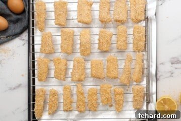 Breaded fish sticks on baking rack over baking sheets.