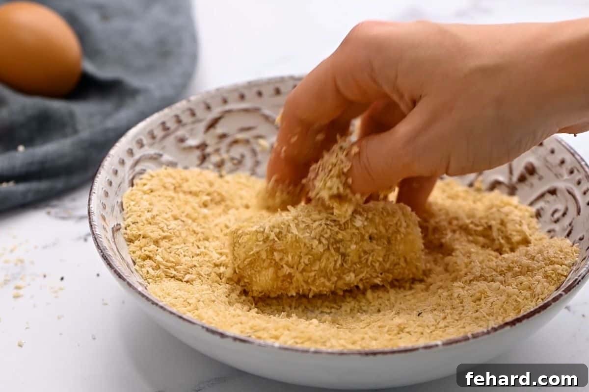 Hand rolling fish stick in panko breadcrumb coating.