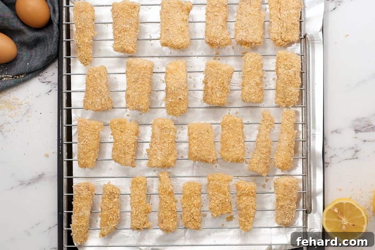 Breaded fish sticks on baking rack over baking sheets.