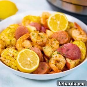 Instant Pot Shrimp Boil made with red potatoes, corn on the cob, and kielbasa in a white platter topped with parsley and fresh lemons next to Instant Pot.