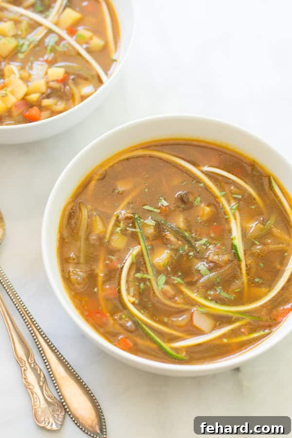 A steaming bowl of vibrant zucchini noodle soup, garnished with fresh herbs, showcasing its rich texture and inviting warmth.