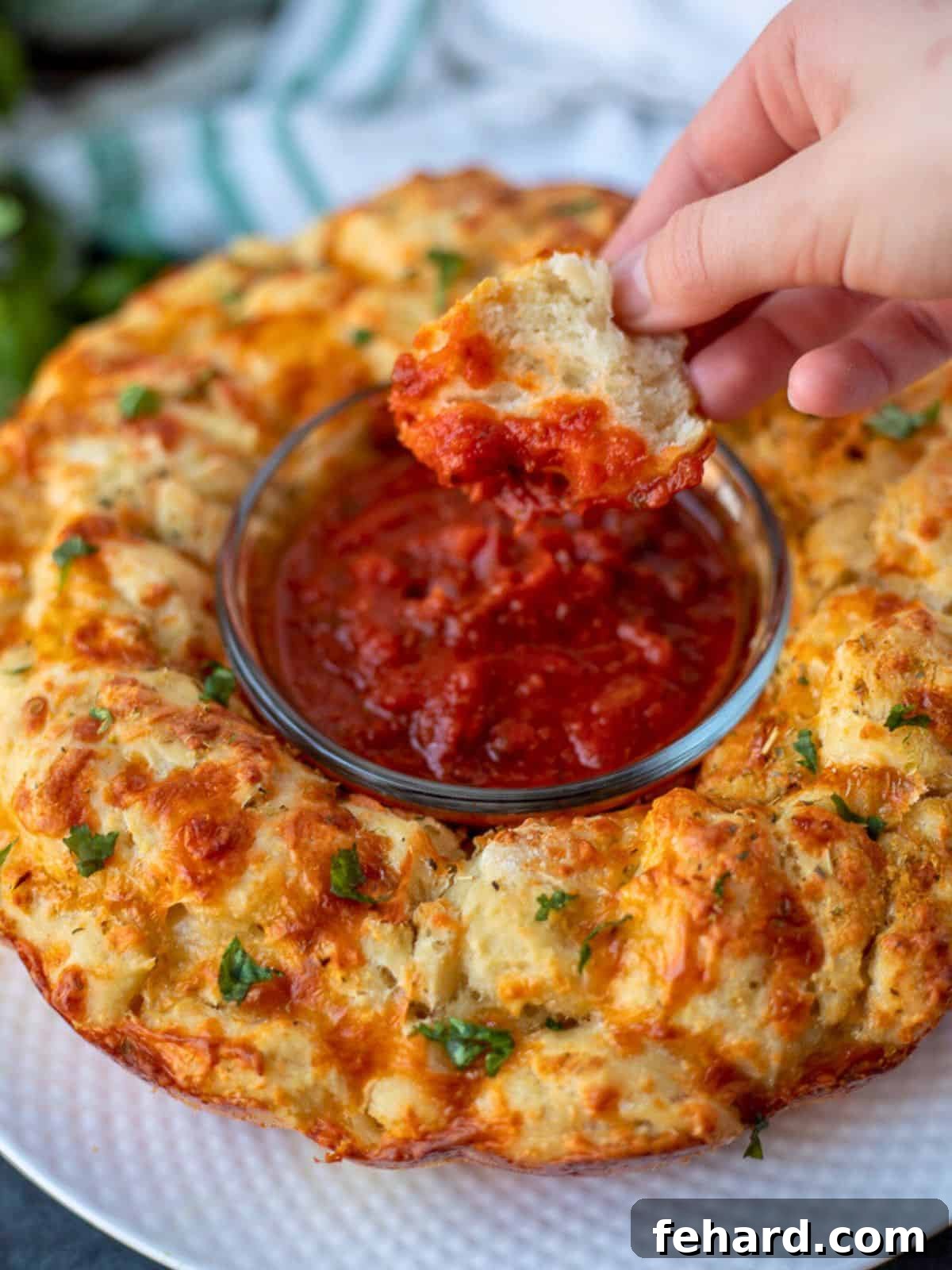 A piece of pull-apart pizza bread being dipped into pizza sauce, showcasing its melty cheese and golden crust.