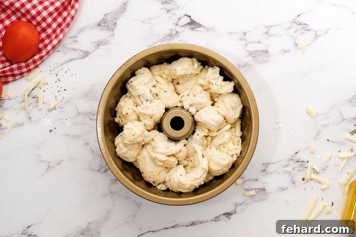 Cheesy pizza dough layered in a greased bundt cake pan, ready to rise and bake into pizza bread.