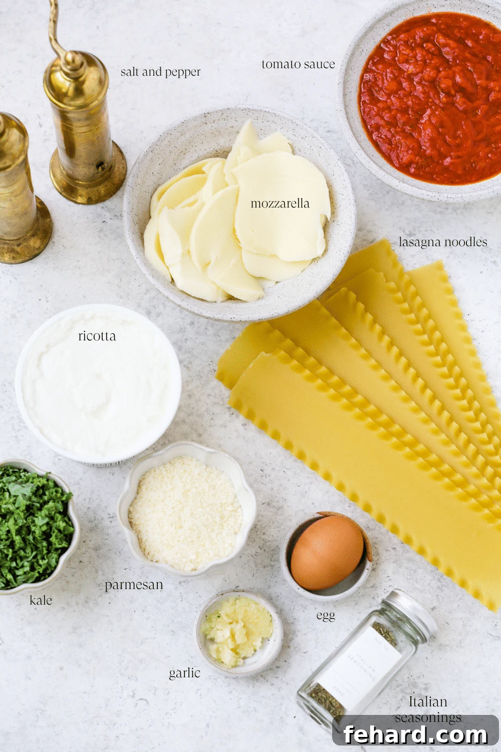 A vibrant display of fresh ingredients for making lasagna roll-ups, including cheese, kale, garlic, and noodles.
