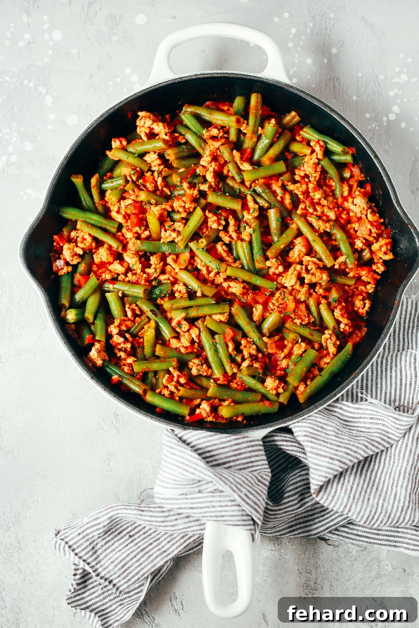 overhead view of a white skillet containing green beans and ground turkey