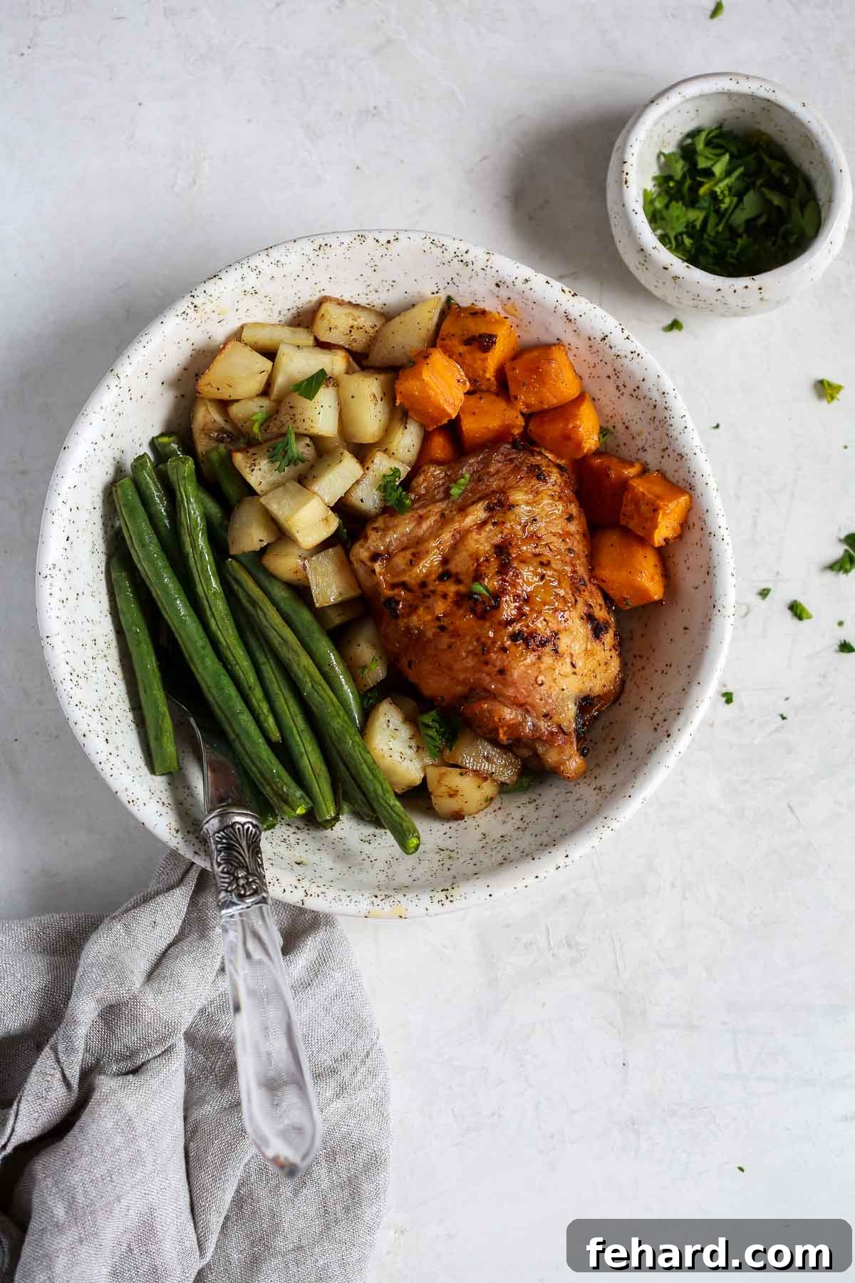 Golden Roasted Chicken and Garden Vegetables 4 Overhead shot of a white bowl filled with beautifully cooked sheet pan chicken and an assortment of roasted vegetables.