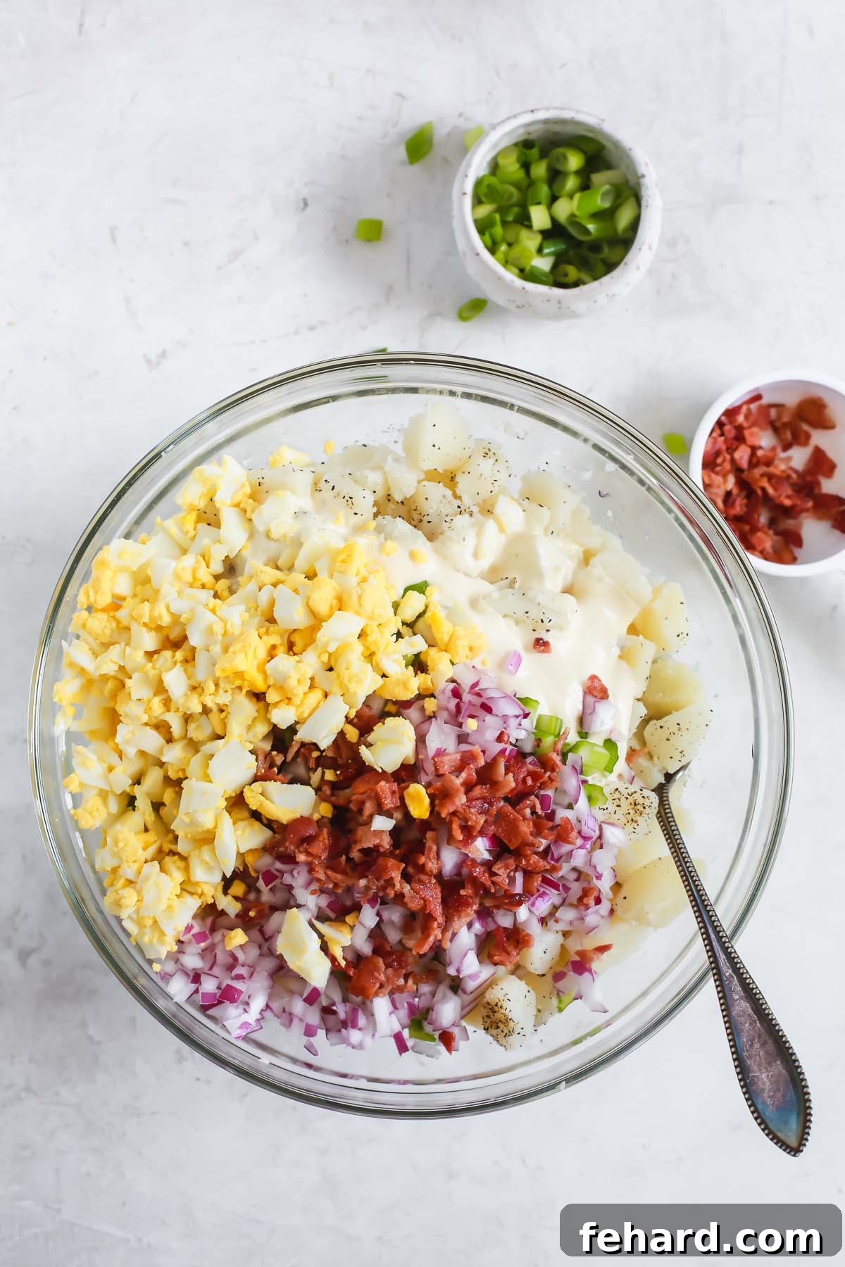 combining mayonnaise, eggs, potatoes, and bacon bits in a bowl