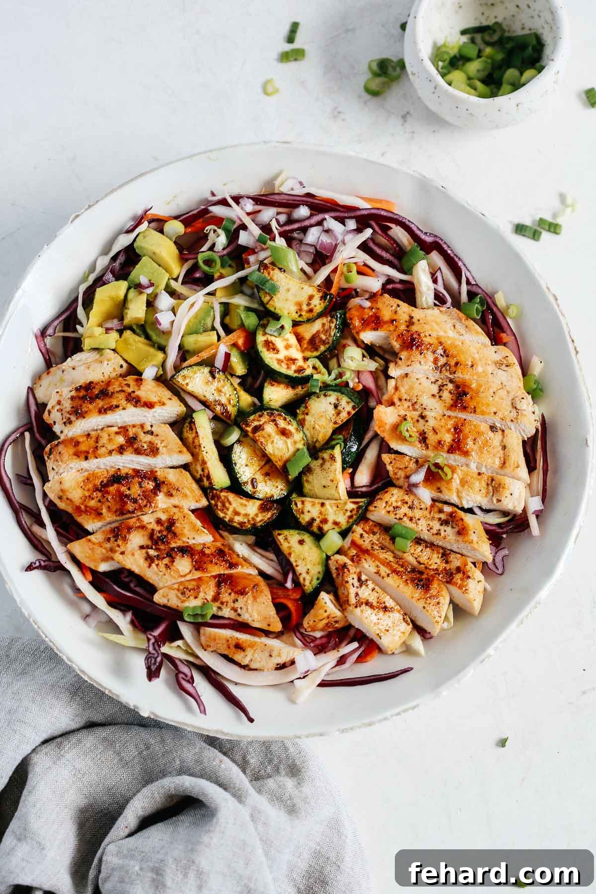 Overhead view of a prepared chicken cabbage salad in a clean white bowl, showcasing the colorful shredded cabbage, carrots, sliced red onion, grilled zucchini, and perfectly cooked chicken strips.
