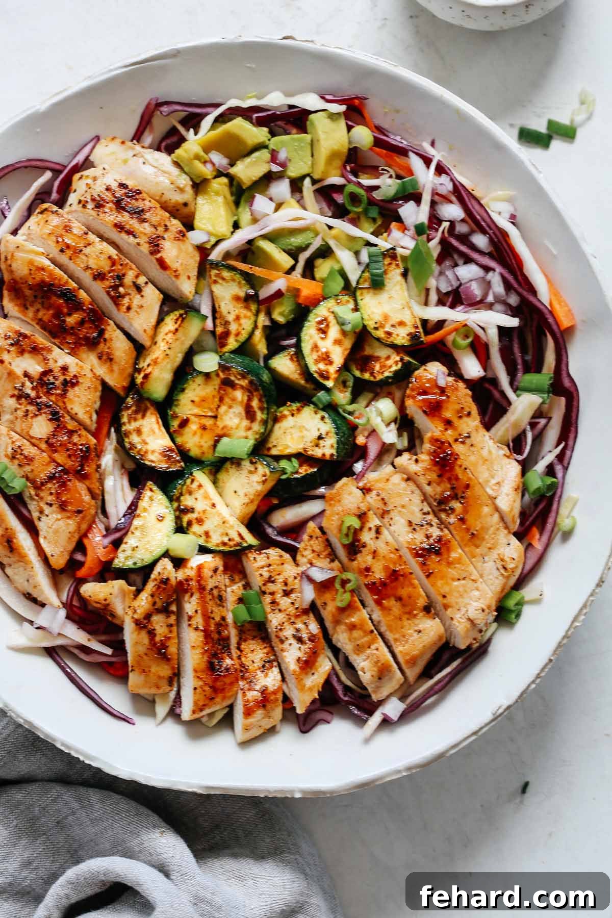 A vibrant close-up of a freshly made chicken cabbage salad in a bowl, highlighting the textures of grilled chicken, shredded cabbage, and colorful vegetables, glistening with dressing.