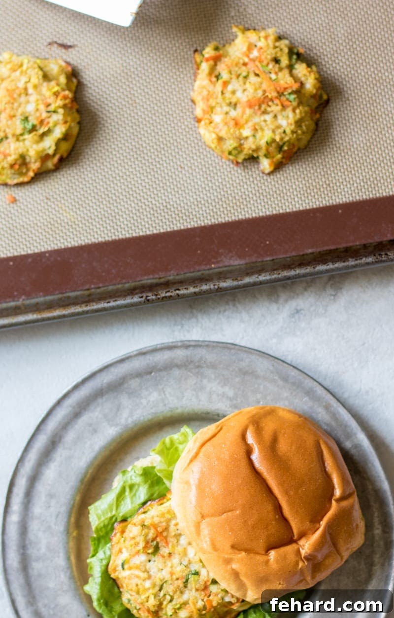Two golden-brown Quinoa Burgers on a baking mat, with one assembled burger on a bun beside them.