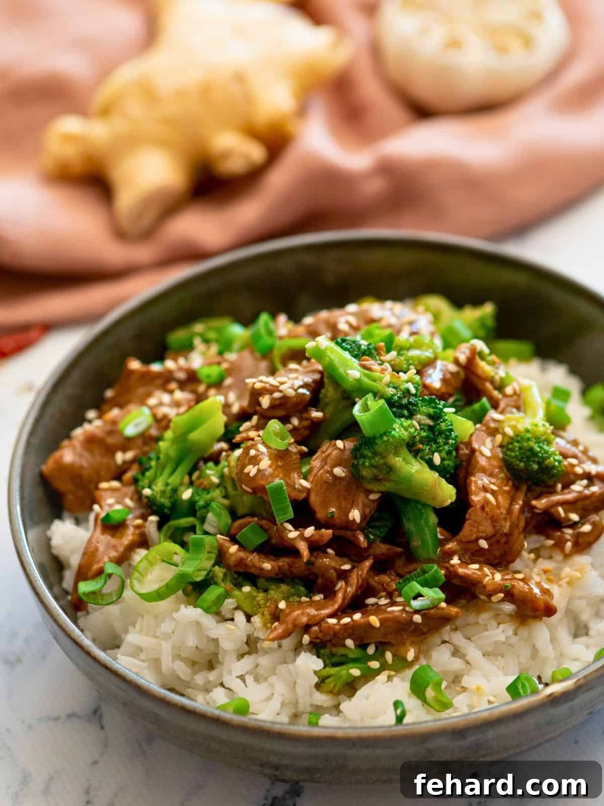 Quick Instant Pot Beef and Broccoli 2 A beautifully plated serving of Instant Pot Beef and Broccoli, garnished with toasted sesame seeds and fresh sliced green onions, resting on a bed of white rice.
