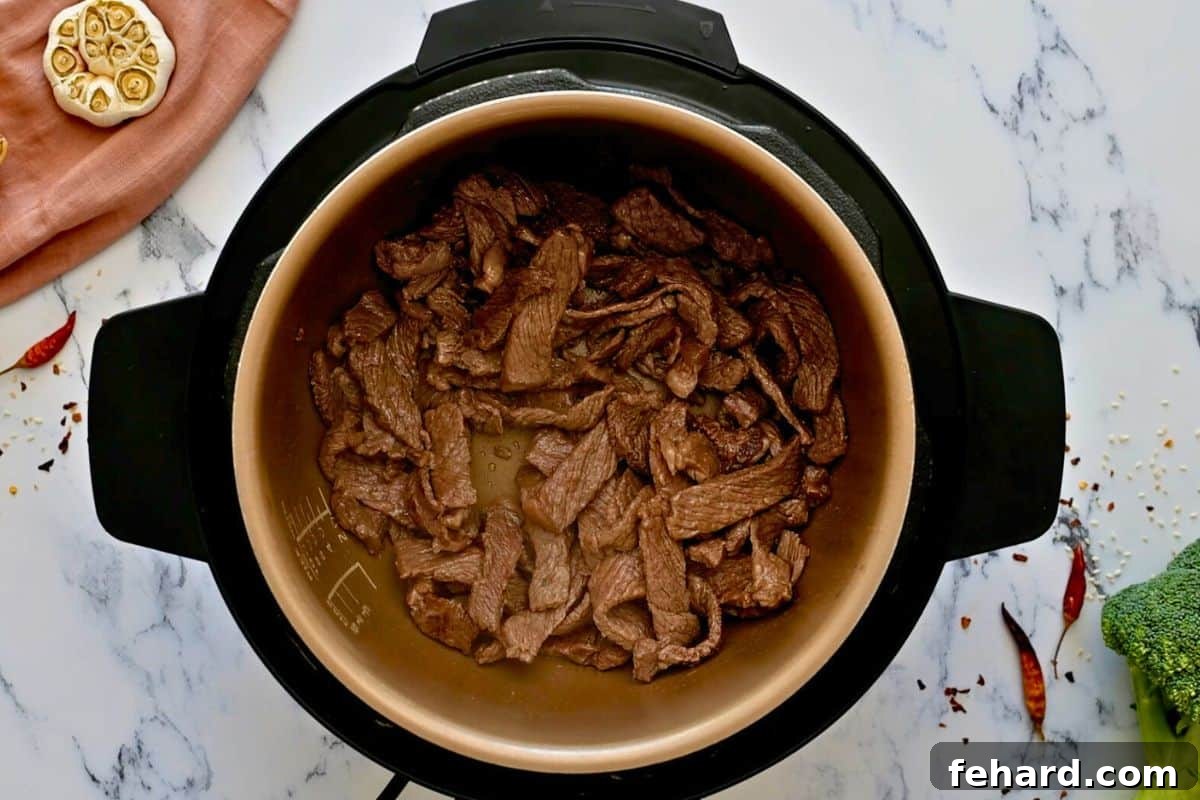 Pressure Cooker Beef and Broccoli Slices of sirloin steak, beautifully browned, inside the Instant Pot's inner pot, with fresh broccoli visible in the background.