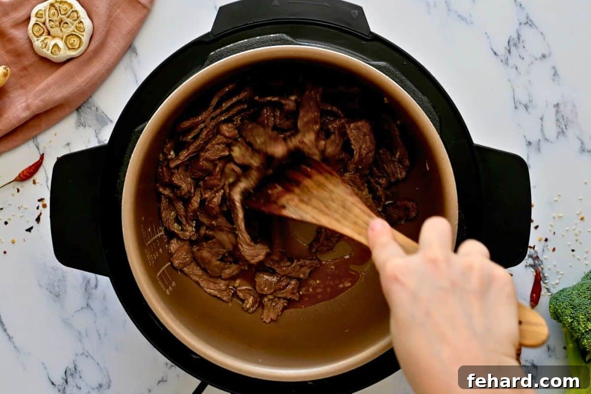 Beef and Broccoli Instant Pot A wooden spoon diligently scraping browned bits from the bottom of the Instant Pot's inner pot after beef has been sautéed and liquid added.