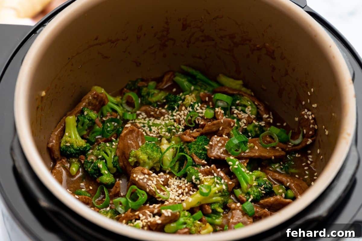 IP Broccoli and Beef Recipe Finished Instant Pot Beef and Broccoli dish, generously topped with sesame seeds and green onions, presented beautifully in the Instant Pot's inner pot.