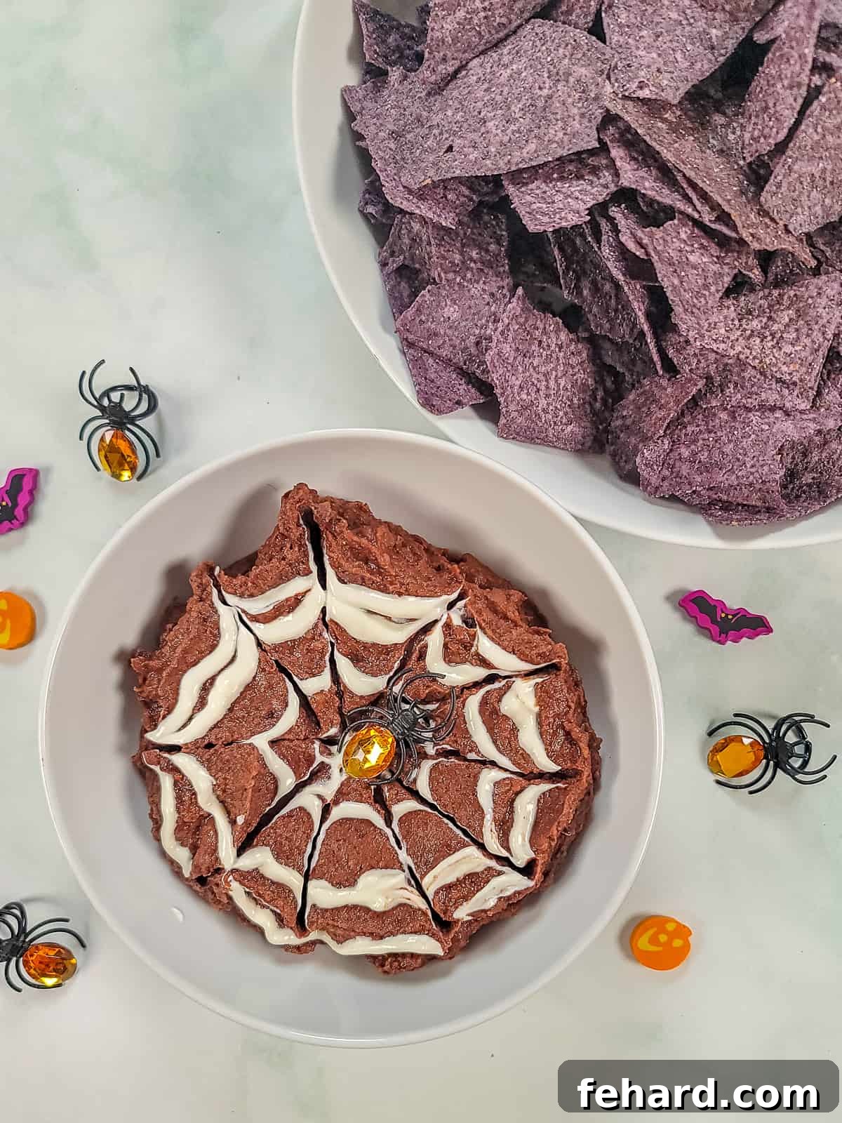 A black bean dip adorned with a white sour cream spider web pattern and a plastic spider ring, ready to be served.